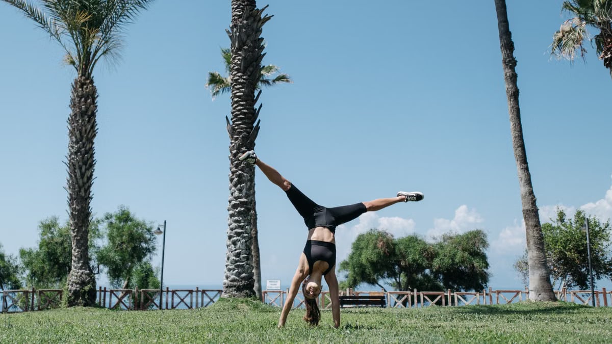 A woman enjoying a cartwheel on a grassy park under clear blue skies, surrounded by palm trees.