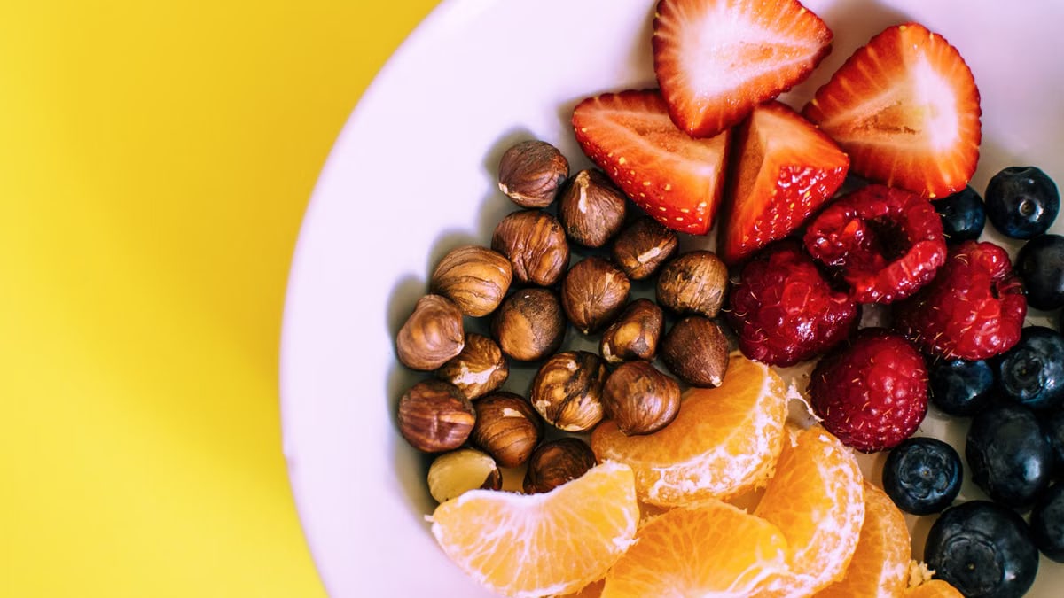 Close-up of a bowl with fresh fruits and nuts against a vibrant yellow backdrop.